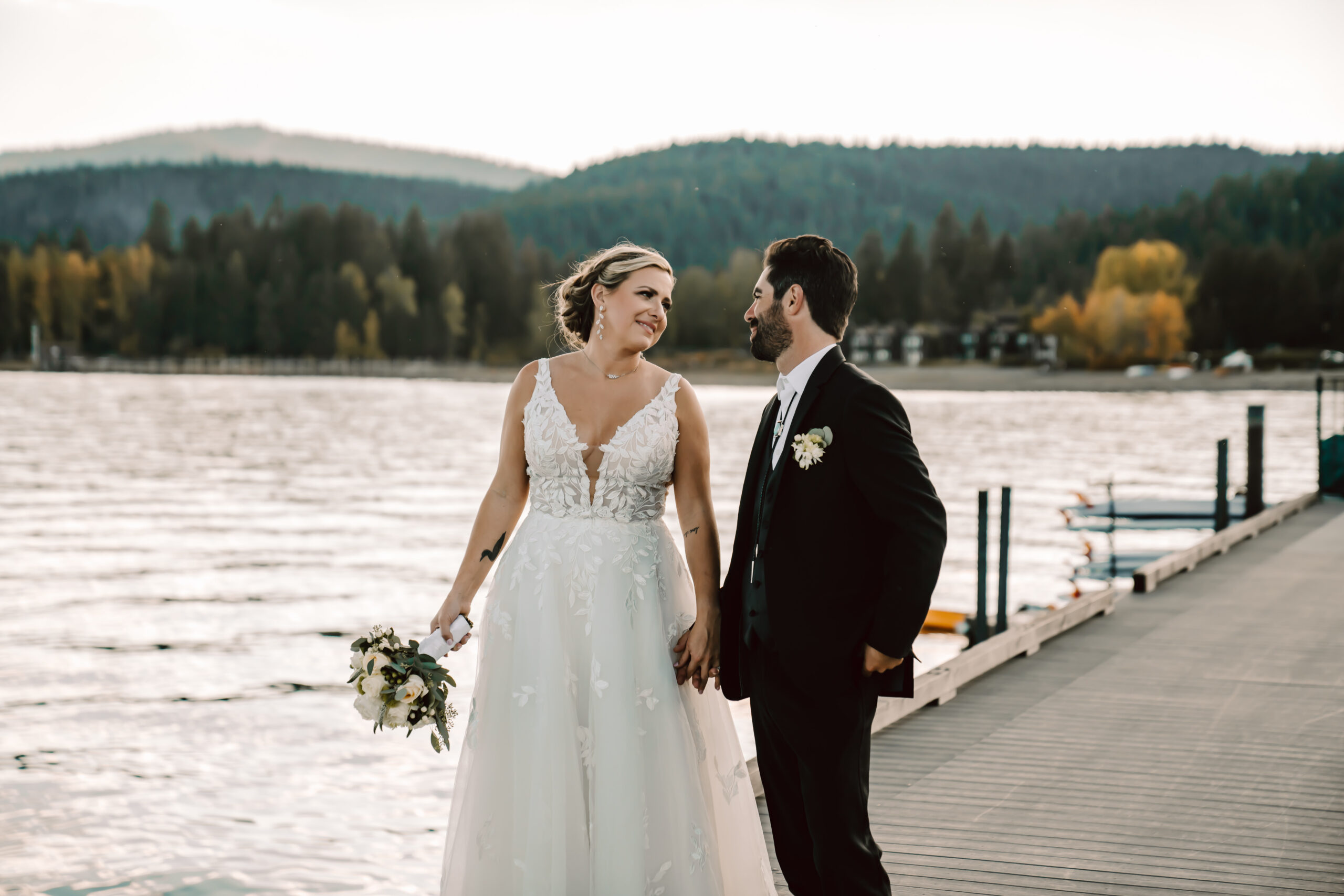 A bride and groom walking on a dock in Lake Tahoe during their wedding day with mountains in the backdrop