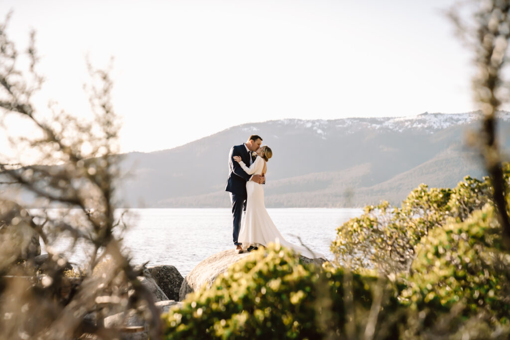 A wedding couple standing on a rock overlooking the mountains and kissing