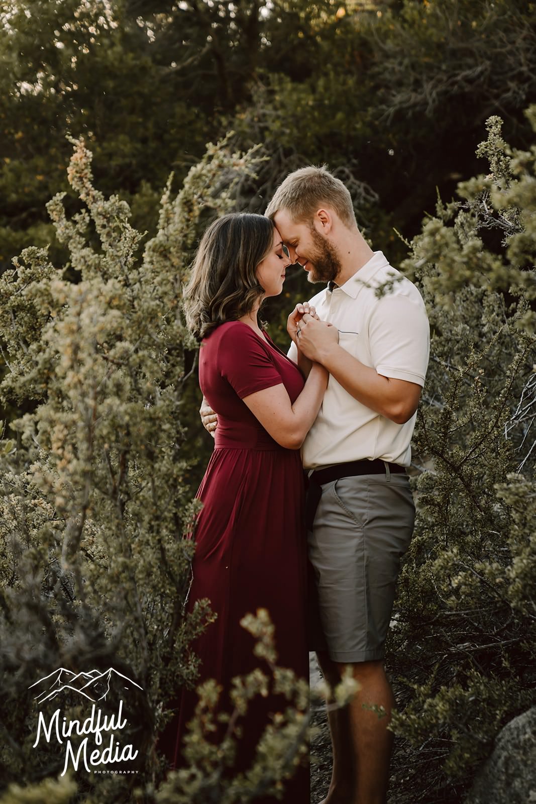 a engaged couple in the trees with their heads together 