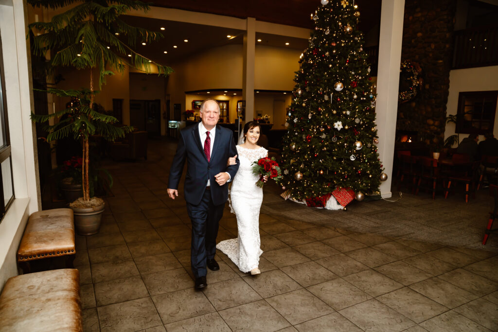 A bride and her dad walking down the eisle with a Christmas Tree in the background