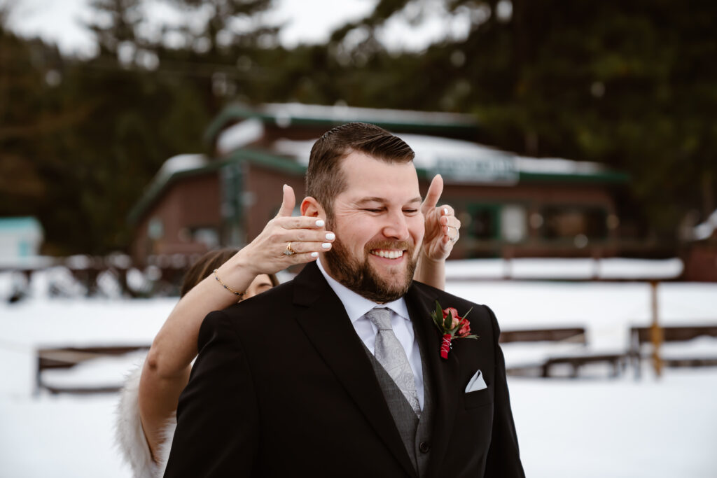 A groom with his eyes closed getting ready for first look in the snow