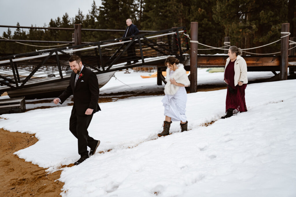 a bride and groom walking in the snow down to the beach on their wedding day