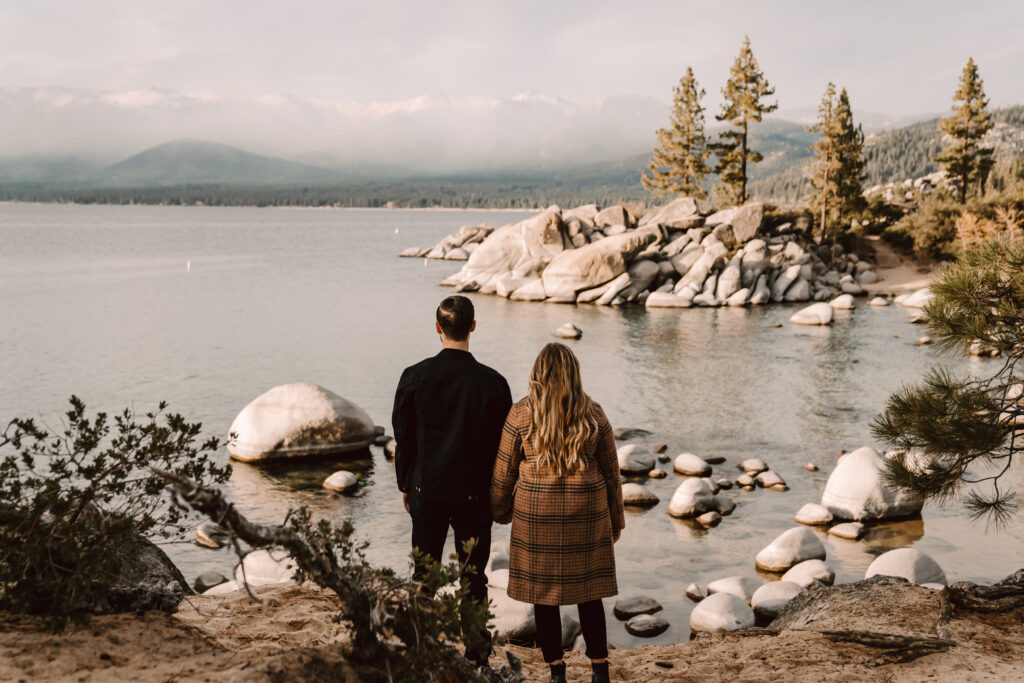  an engaged couple looking out over Sand Harbor on their engagement photo session