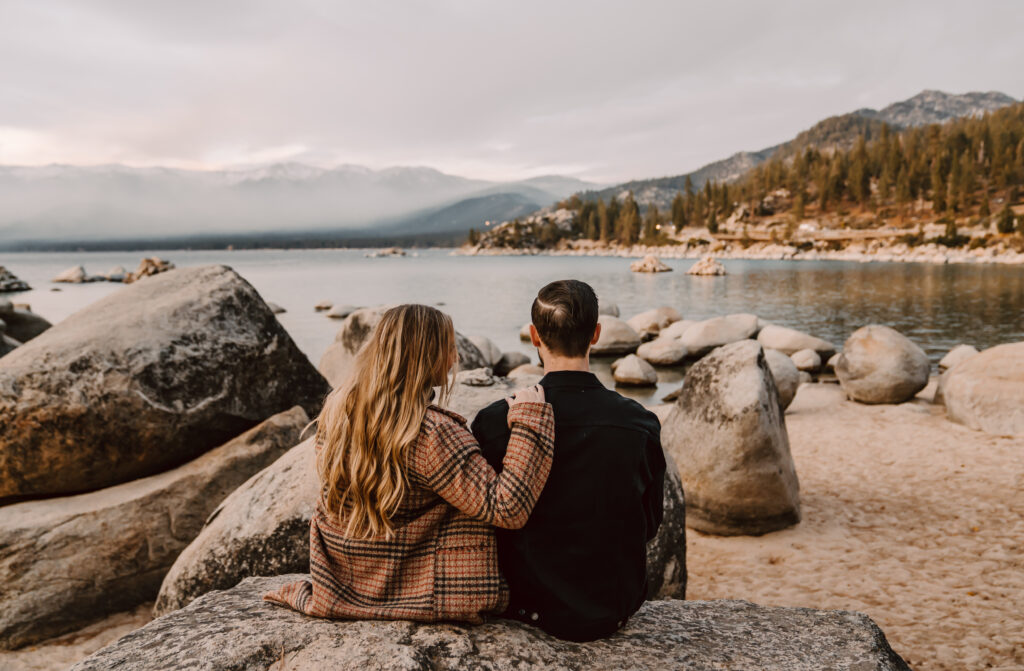 a couple sitting on a boulder looking out onto the water of Lake Tahoe