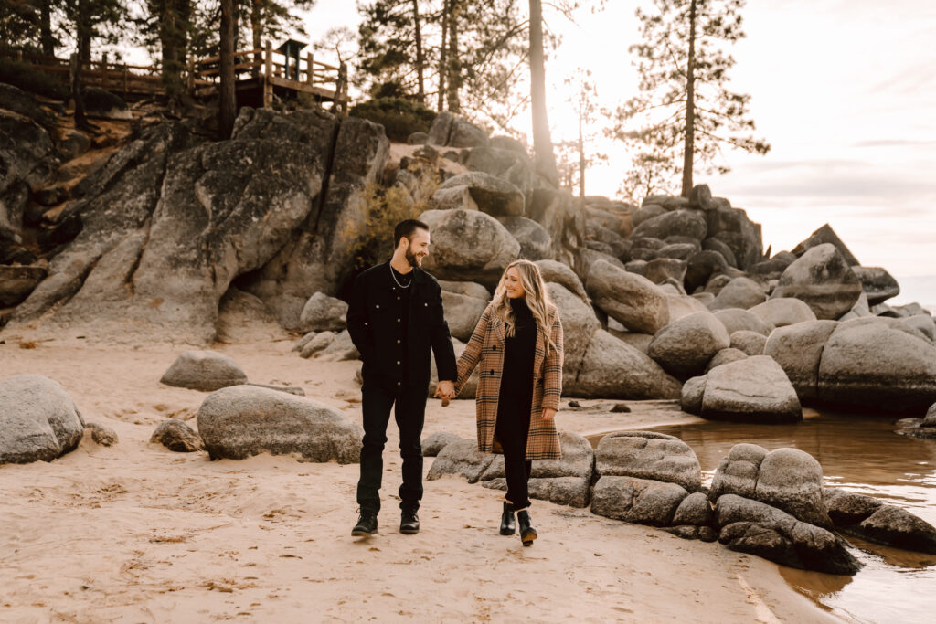 a engaged couple walking on the beach at Sand Harbor with boulders in the backdrop