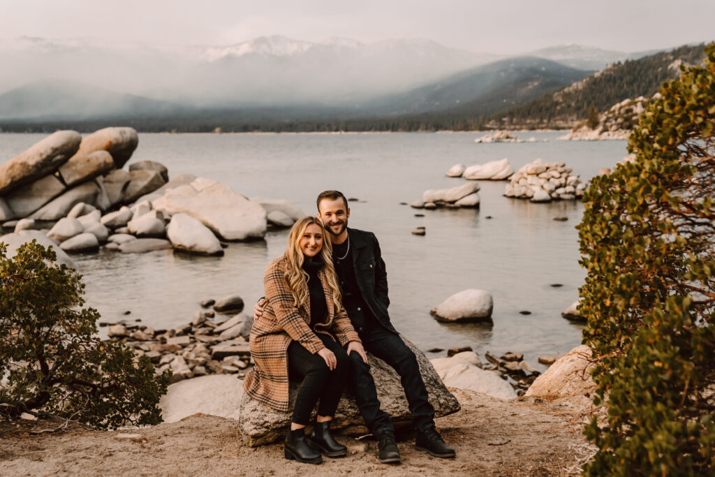 a couple sitting on a rock with sand harbor and the mountains in the backdrop