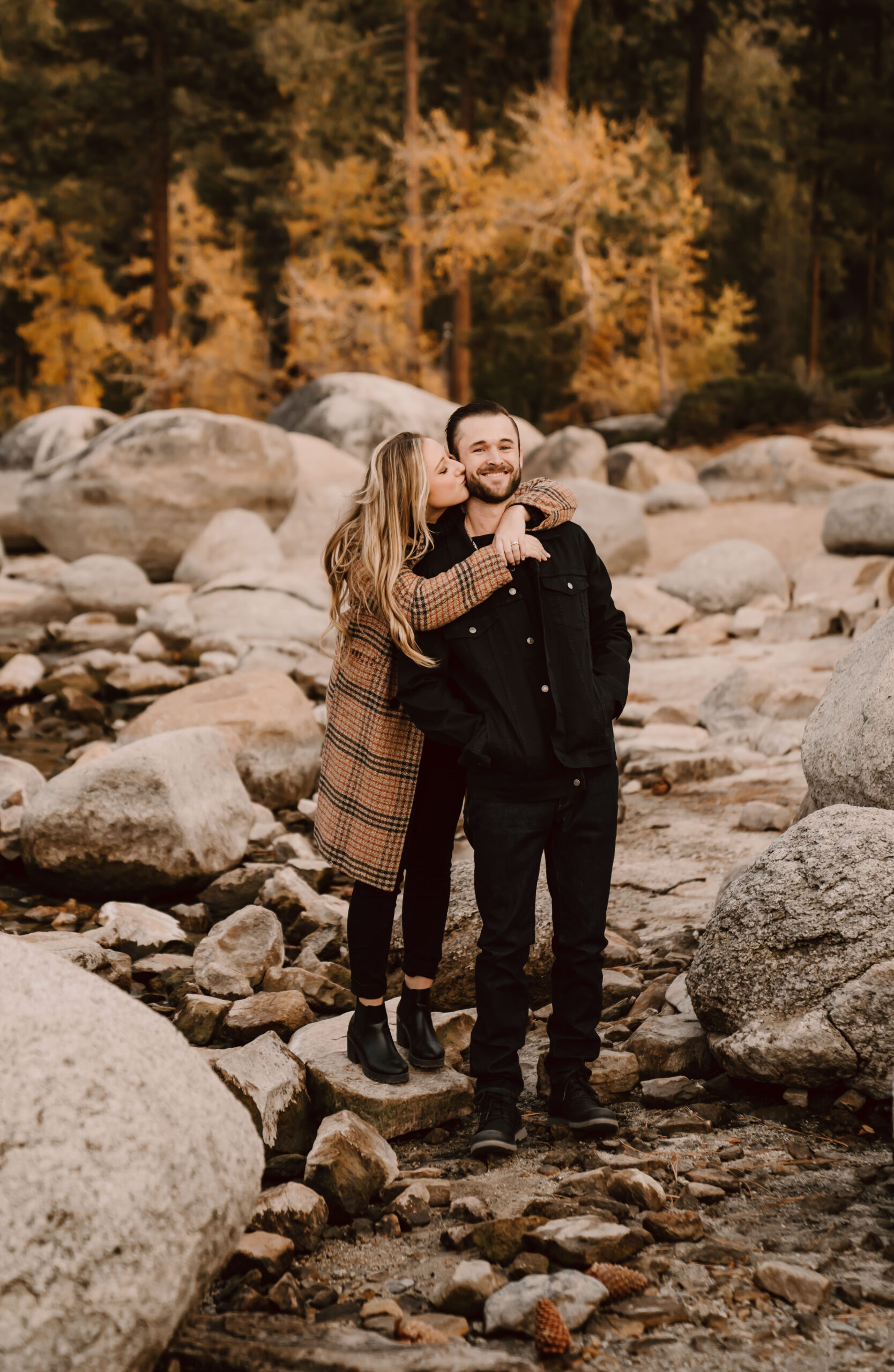 A girl kissing her fiance and standing on some rocks at Sand Harbor in Tahoe