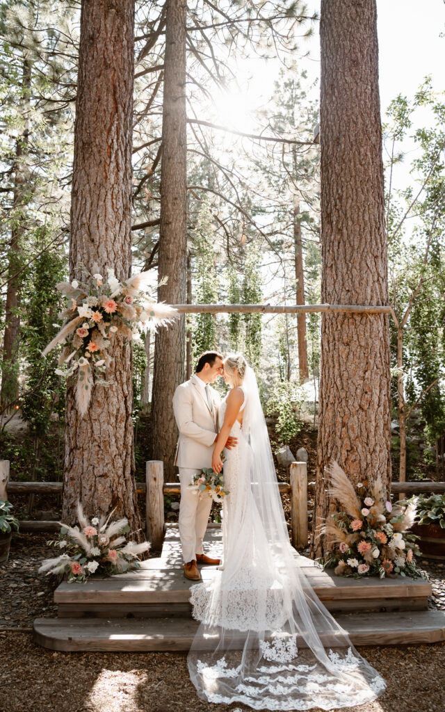 The bride and groom standing under the arch surrounded by tall trees in Lake Tahoe