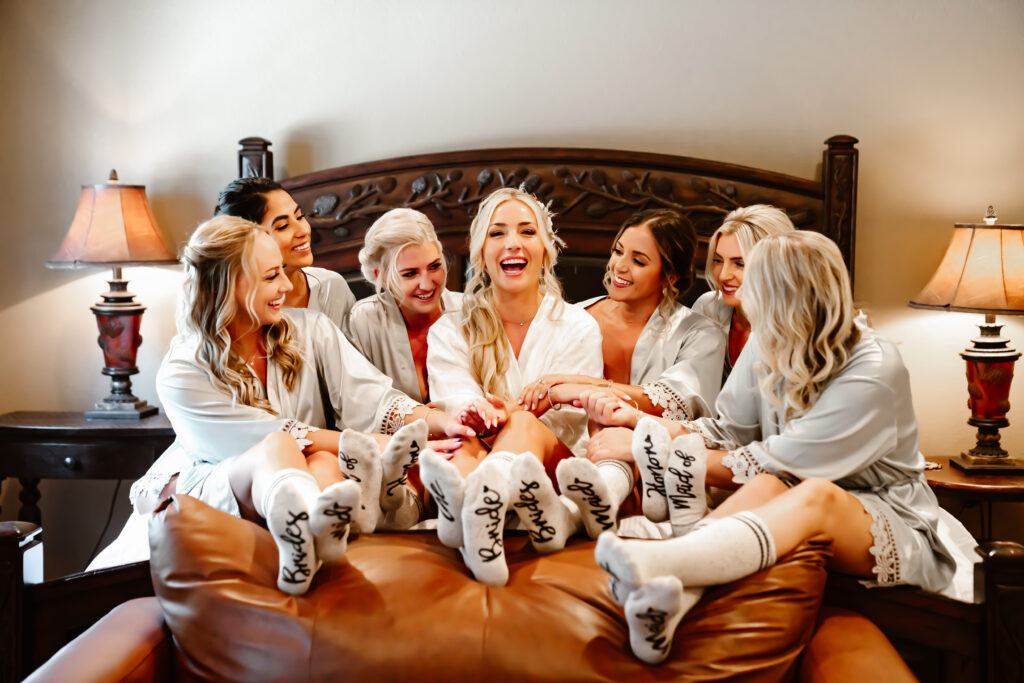 A bride and her bridesmaids sitting on the bed while they are getting ready for their wedding day