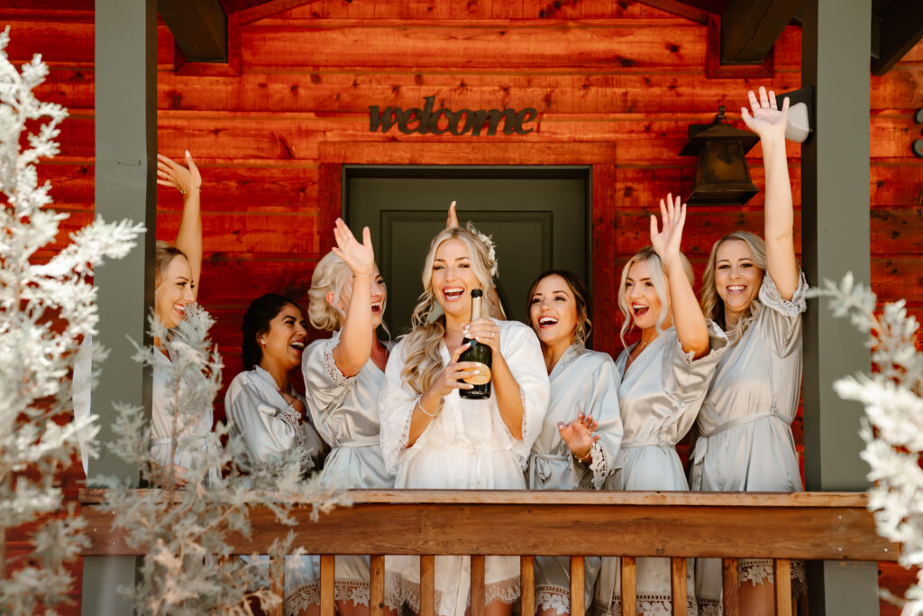 A bride popping champagne with her bridesmaids on the porch of her airbnb in Tahoe for her wedding day