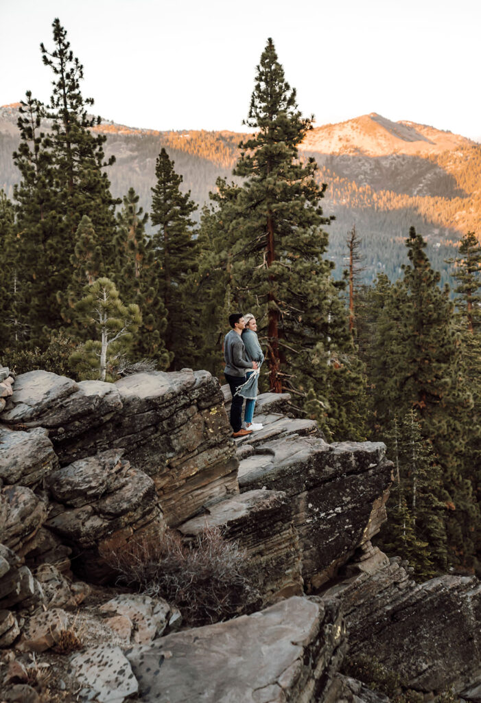 a couple standing on the edge of the mountain looking out onto the sunset in Lake Tahoe