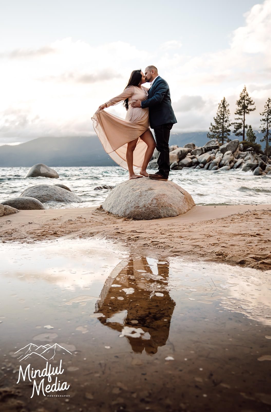 a reflection shot of a couple standing on a boulder and kissing for their engagement photos in Lake Tahoe