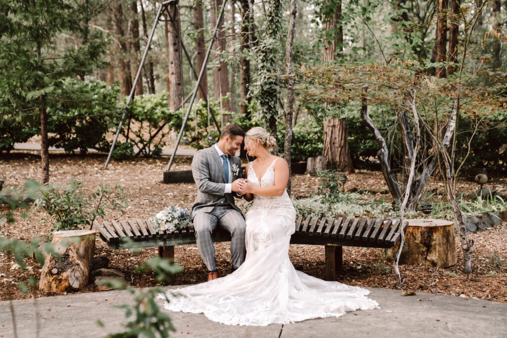 a bride and groom sitting on a bench surrounded by forest on their wedding day