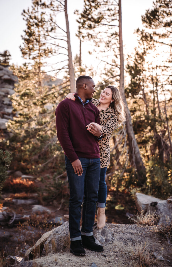 A engaged couple smiling at each other in the trees near truckee
