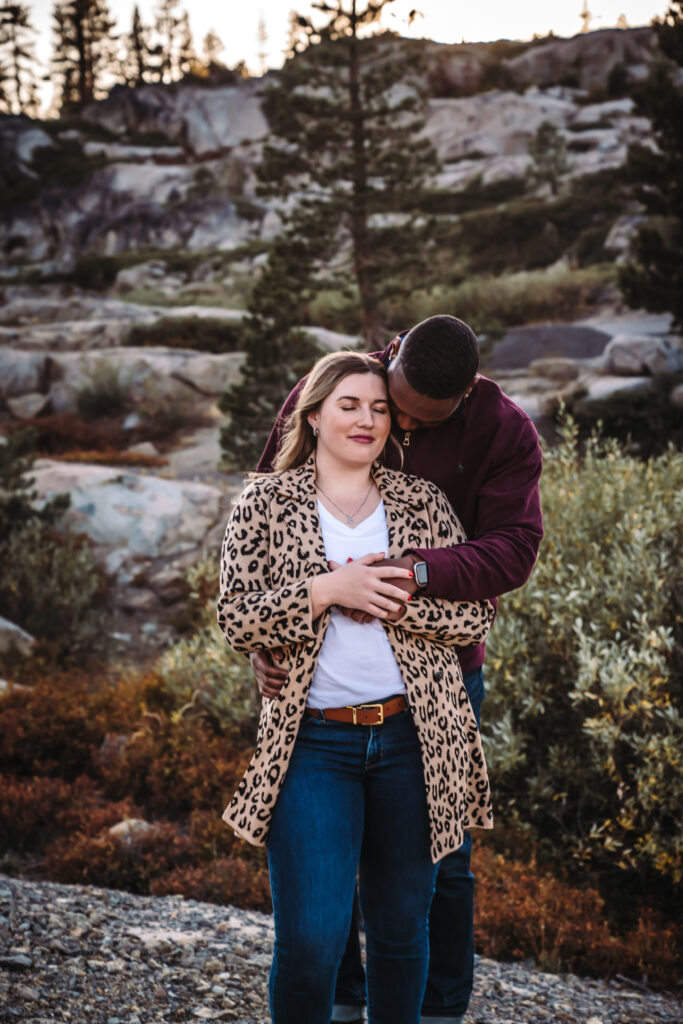 a guy kissing his fiance in front of the mountains in truckee