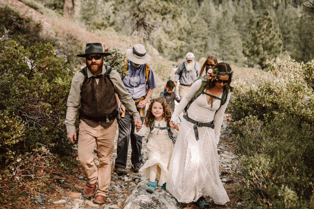 a bride and groom hiking with their friends and family to their ceremony location in the outdoors