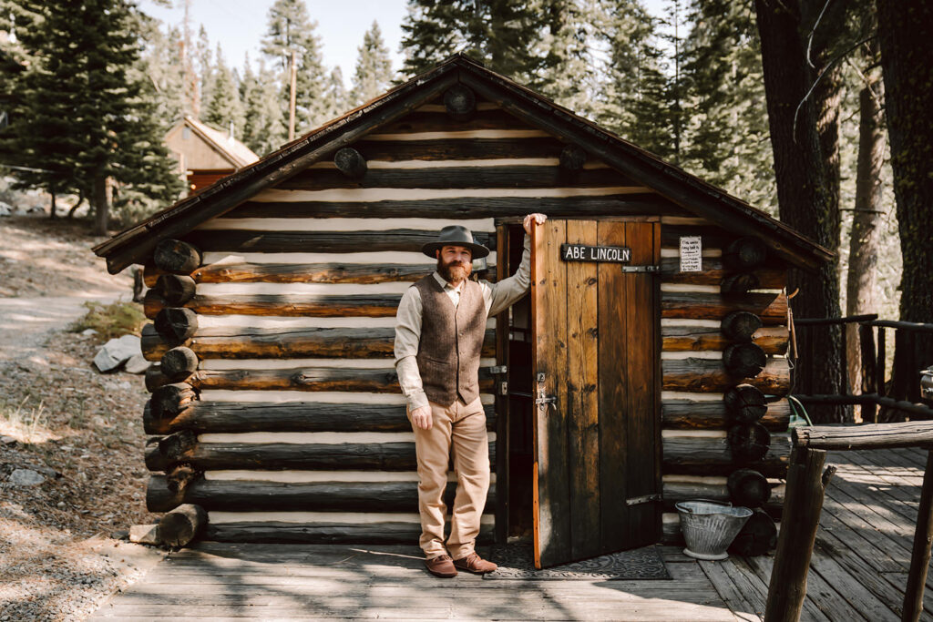 a groom standing next to his rustic cabin getting ready for his elopement