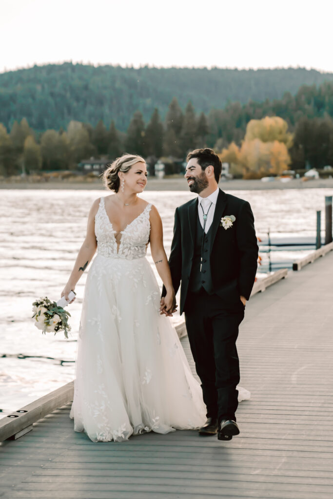 A wedding couple holding hands and walking down the dock overlooking the mountains of Lake Tahoe on their wedding day