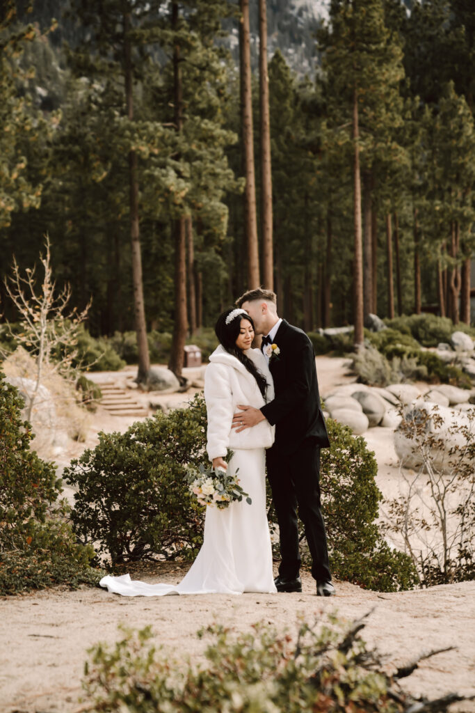 A groom kissing his bride in front of the forest trees in Tahoe on their wedding day