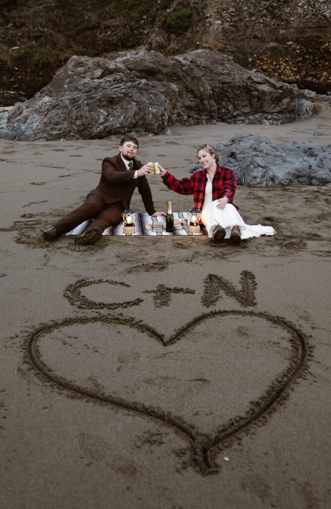 a wedding couple toasting and sitting on a blanket having a picnic on the beach for their elopement day at Enderts Beach 