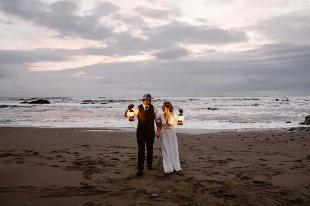 an elopement couple walking on the beach at sunset holding lanterns on their elopement day