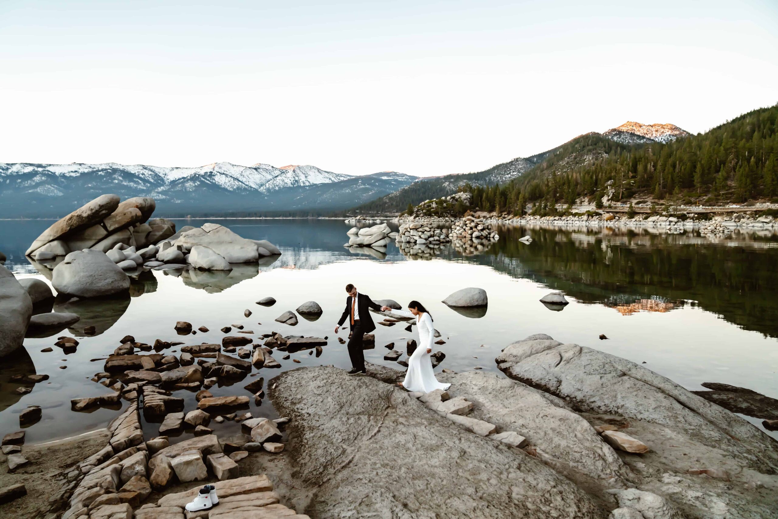 A groom helping his bride jump over rocks in Sand Harbor in Lake Tahoe for their elopement day in the mountains