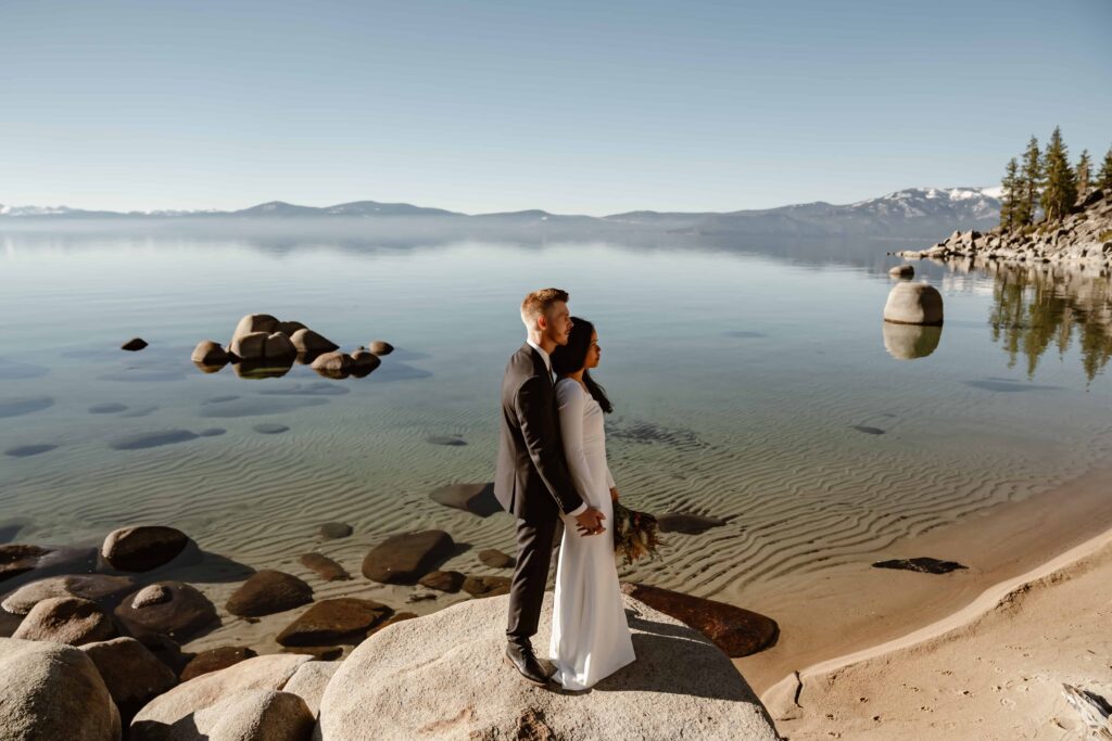 a groom holding his bride and standing on a rock overlooking lake Tahoe