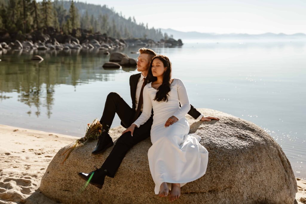 a bride and groom sitting on a rock in front of Lake Tahoe for their elopement day