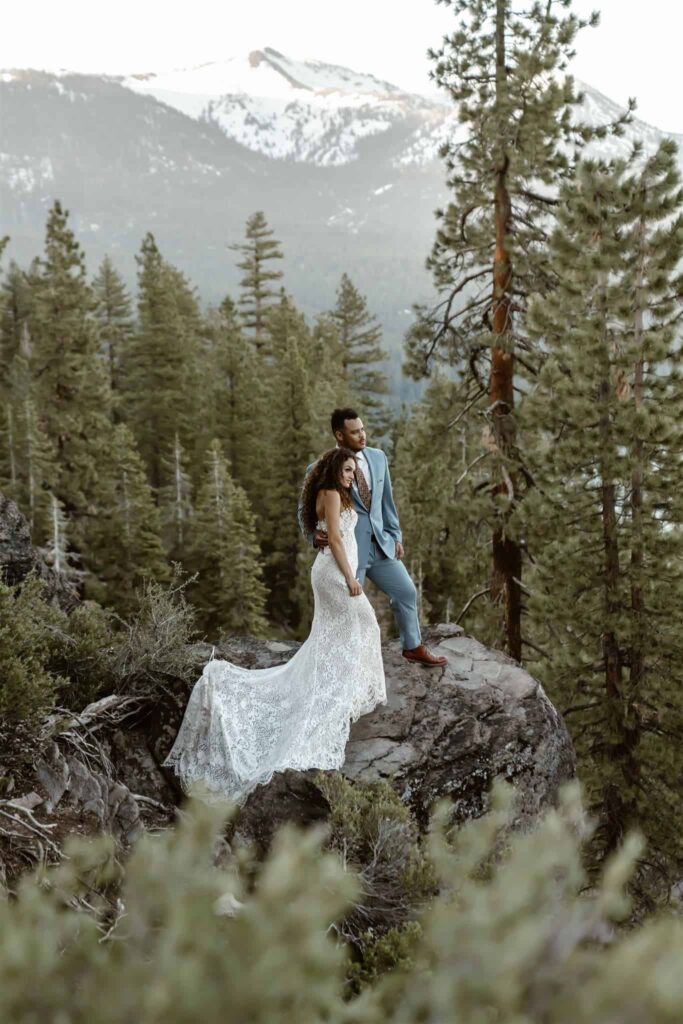 A wedding couple standing on the edge of a cliff overlooking the mountains on the Stateline Fire Lookout trail in Lake Tahoe