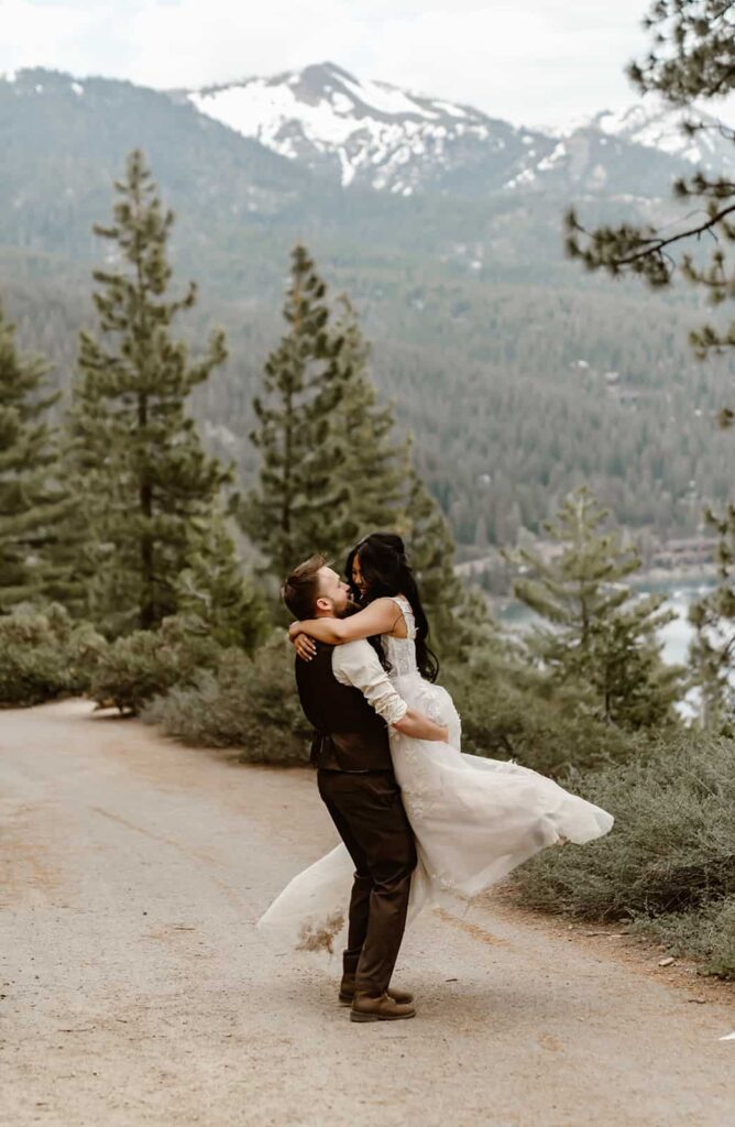 A groom holding his bride in the air and swinging her around in front of a mountain backdrop for their Lake Tahoe Elopement