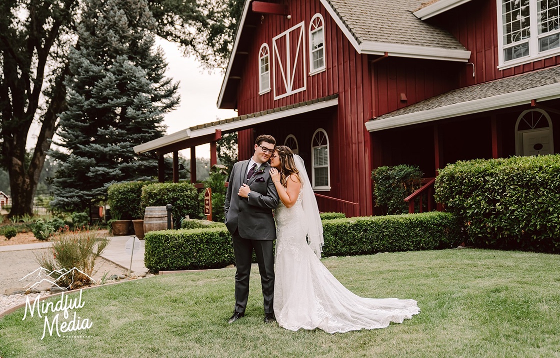 Bride and groom in front of red barn at Rough and Ready Vineyards