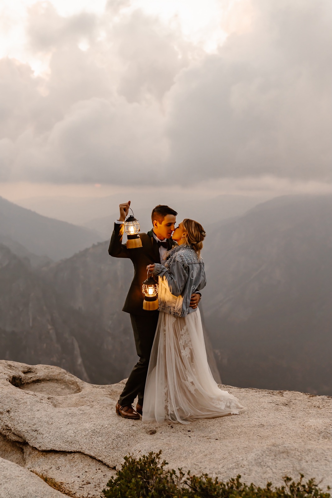 Bride and groom kiss while holding lanterns at Taft Point at sunset