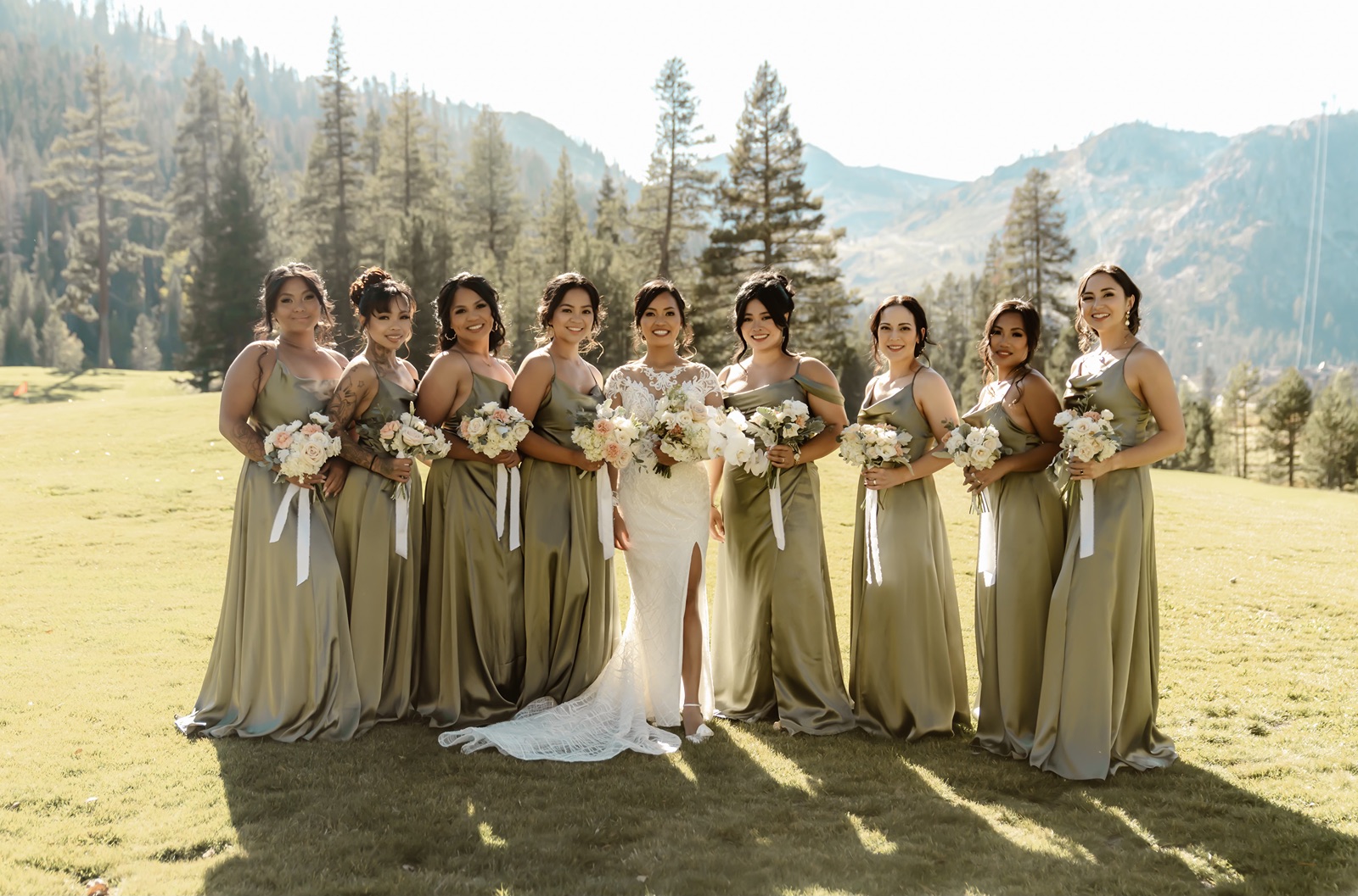 Bridesmaids in green satin dresses smile with the mountains as the backdrop