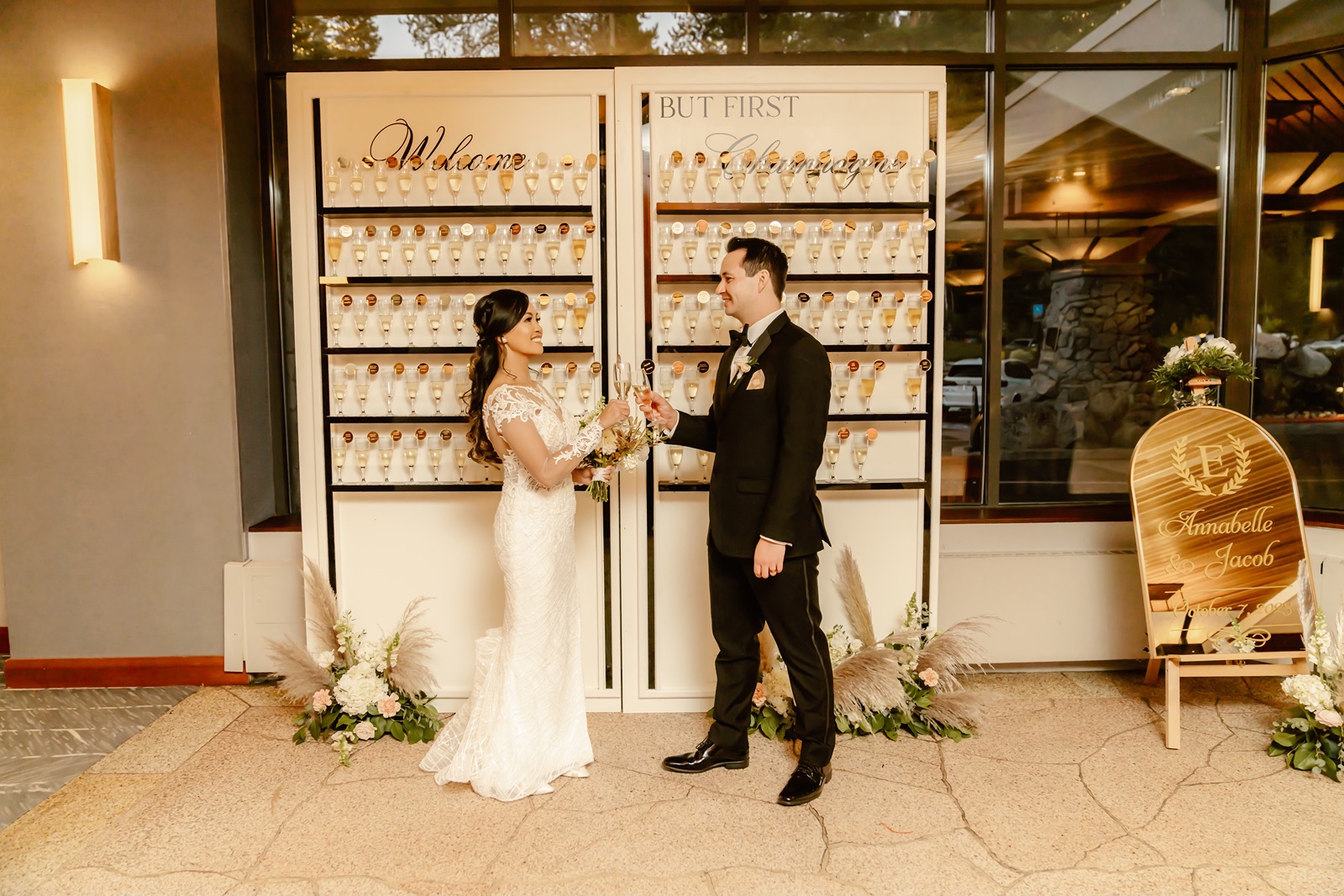Bride and groom cheers in front of their Champagne wall wedding seating chart