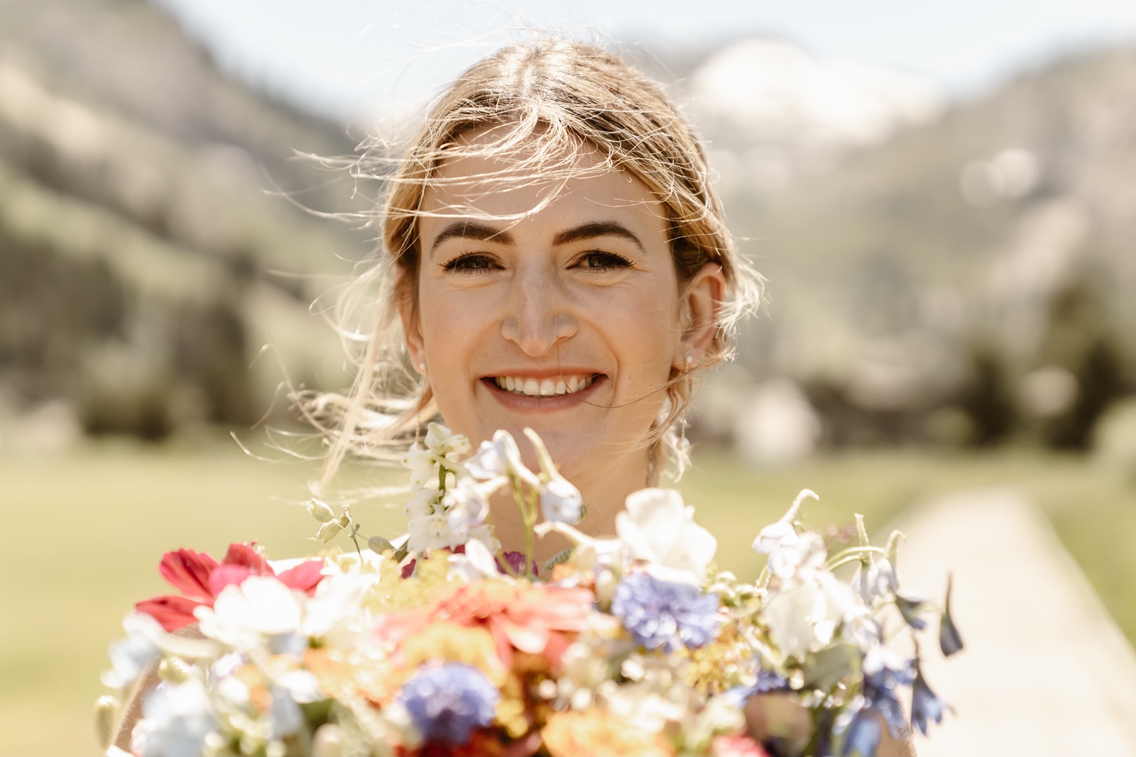 Bride smiles while holding a colorful bouquet close to her face