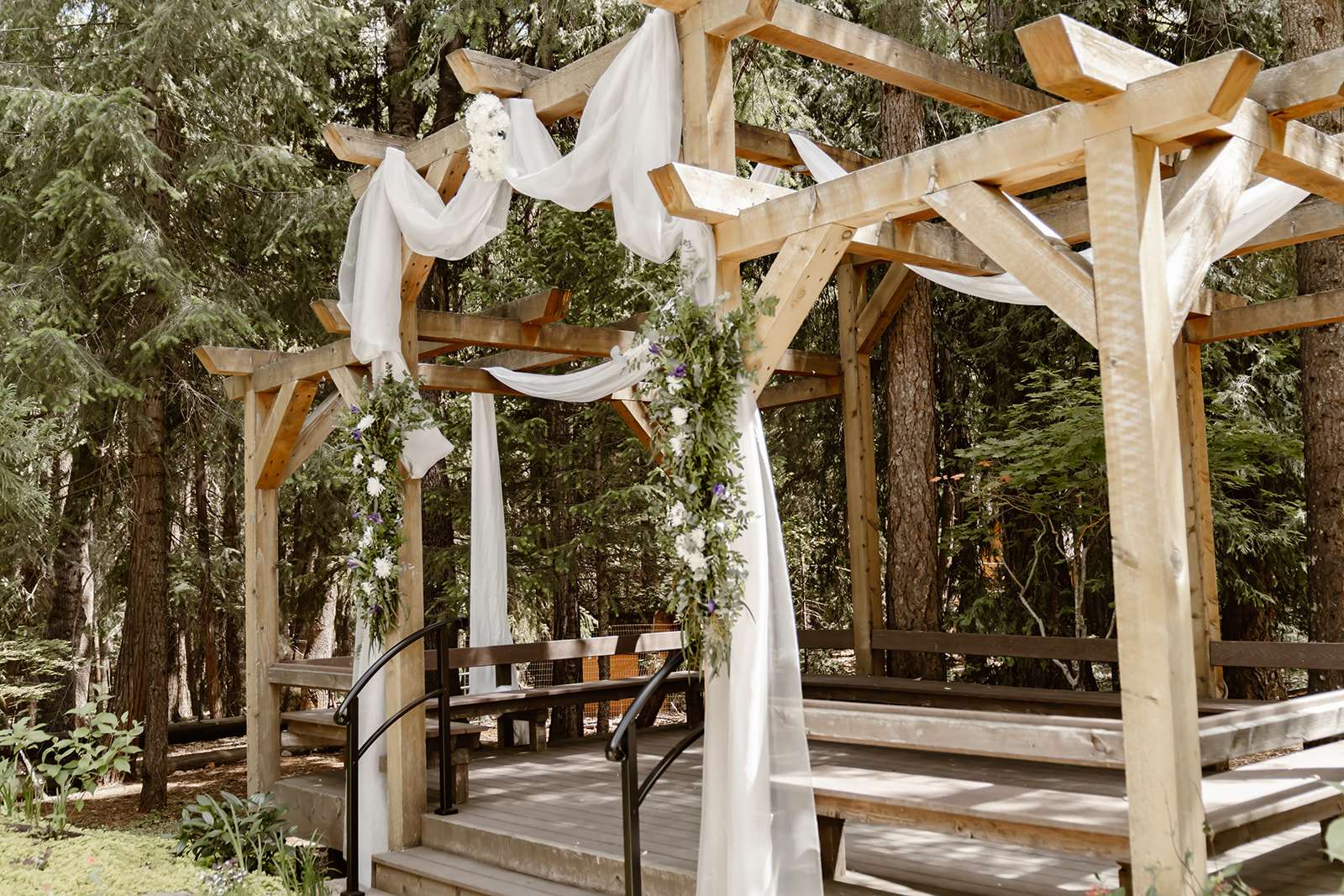 Wedding ceremony pergola draped in white fabric and greenery