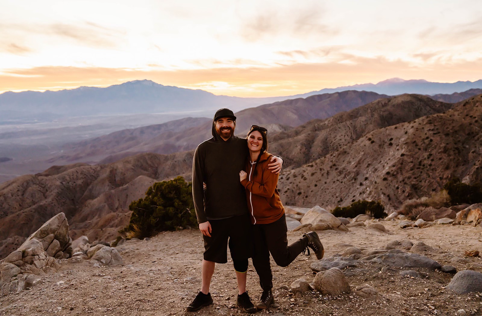 Husband and wife photo and video team pose with mountain backdrop