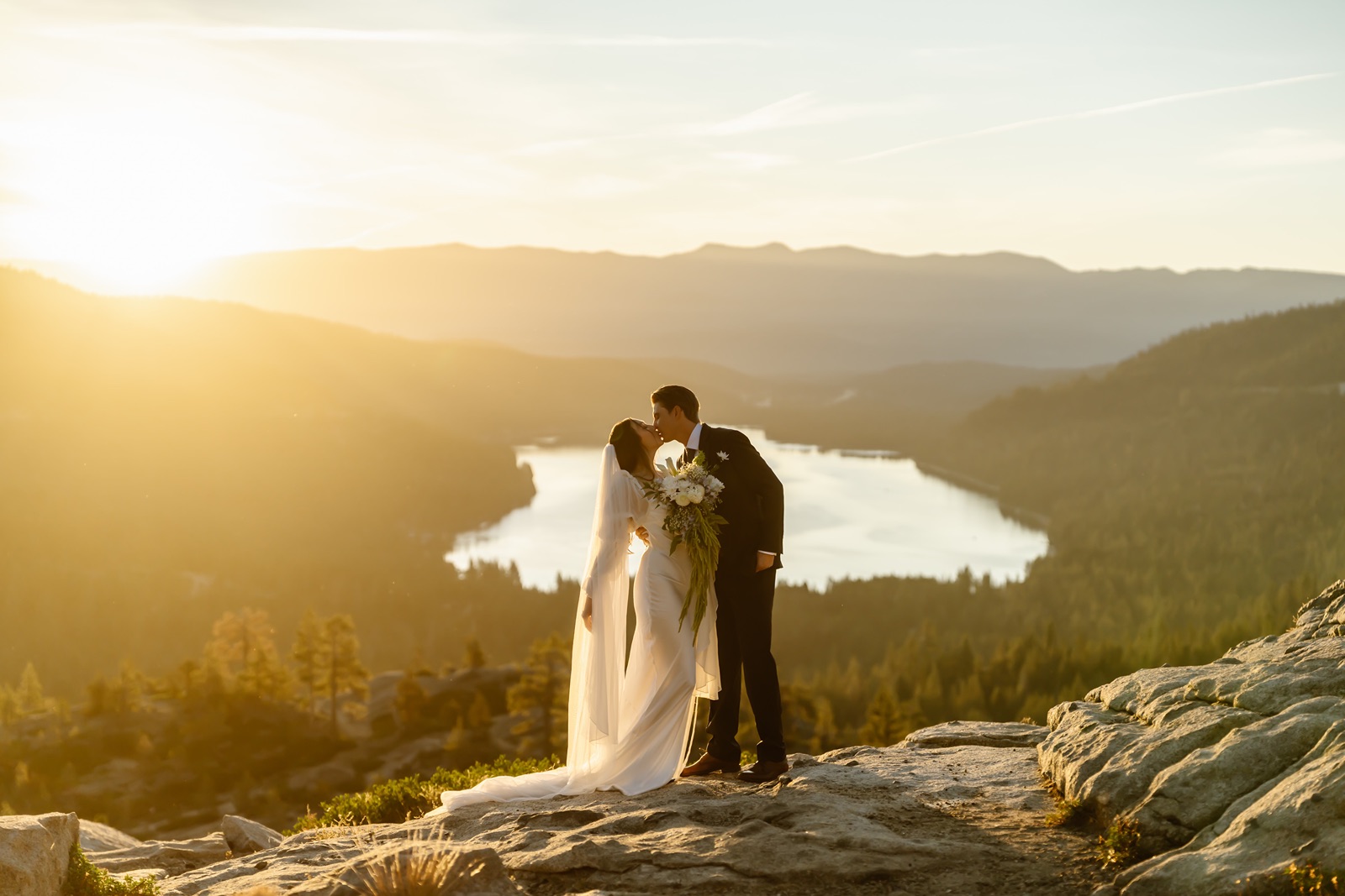 Bride and groom kiss as the sun rises behind them at. Donner Lake Overlook