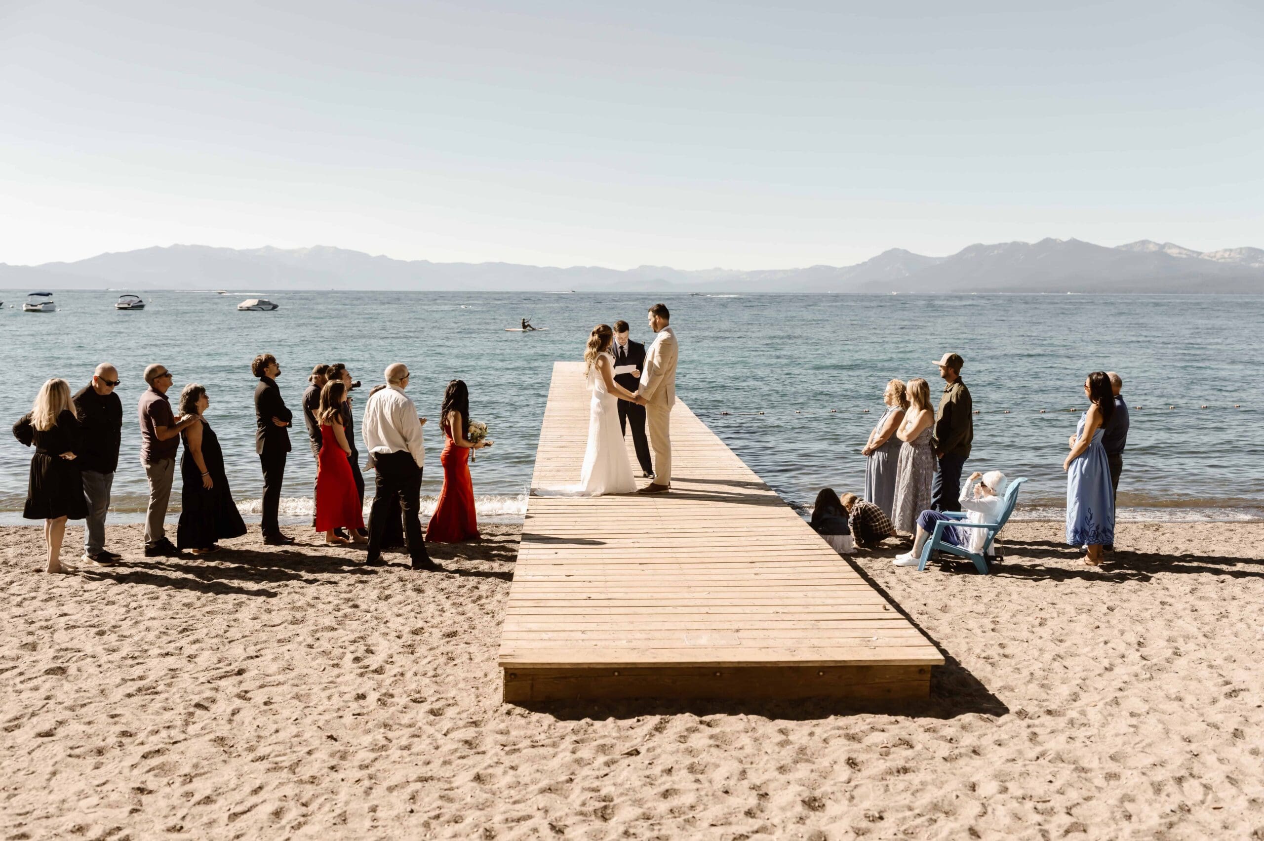 Lake Tahoe elopement ceremony on a wooden dock with the couple exchanging vows as friends and family gather along the beach.