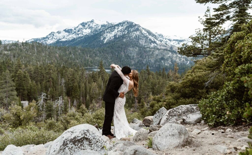 Newlywed couple kissing at a rocky Lake Tahoe overlook with snow-covered mountains in the background