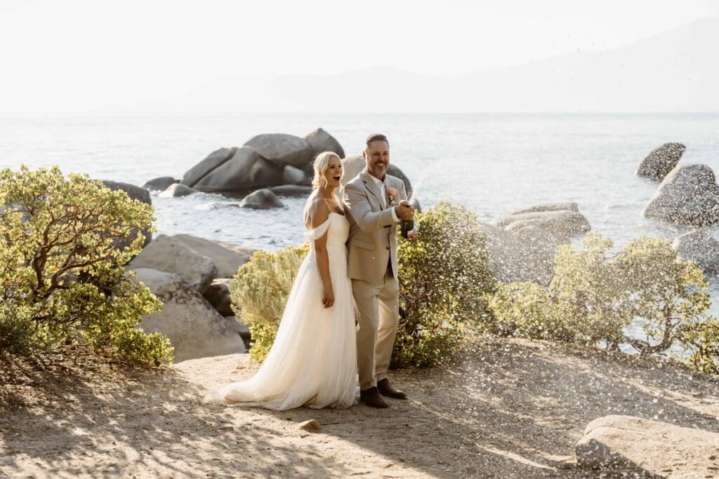 Lake Tahoe Elopement Guide 6 Lake Tahoe elopement couple celebrating with champagne beside the water at Sand Harbor, surrounded by granite boulders and golden light.