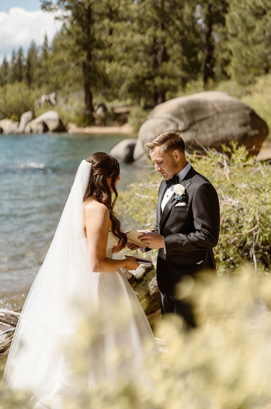 Bride and groom embracing beside the water at Zephyr Cove during their Lake Tahoe elopement, with pine trees and granite boulders along the shoreline.